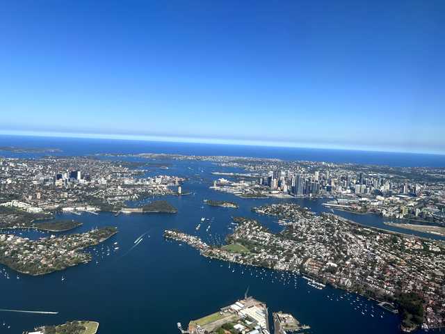 オーストラリア・シドニー湾を上空から撮影した風景。オペラハウスや市街地の高層ビル群、青い海が広がるパノラマ